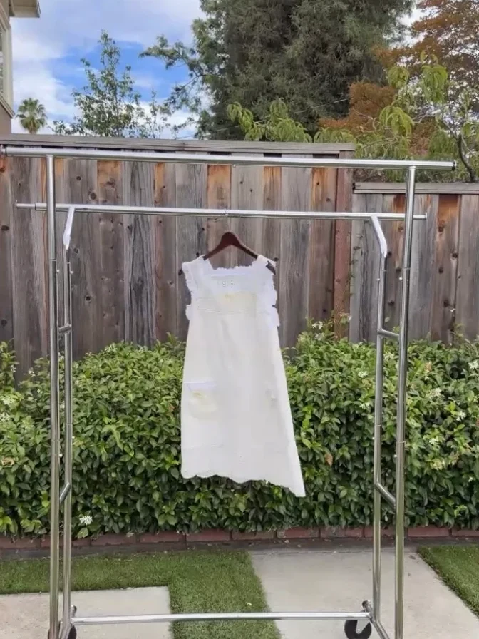 A cream sleeveless dress with ruffled straps, hanging on a garment rack in a garden